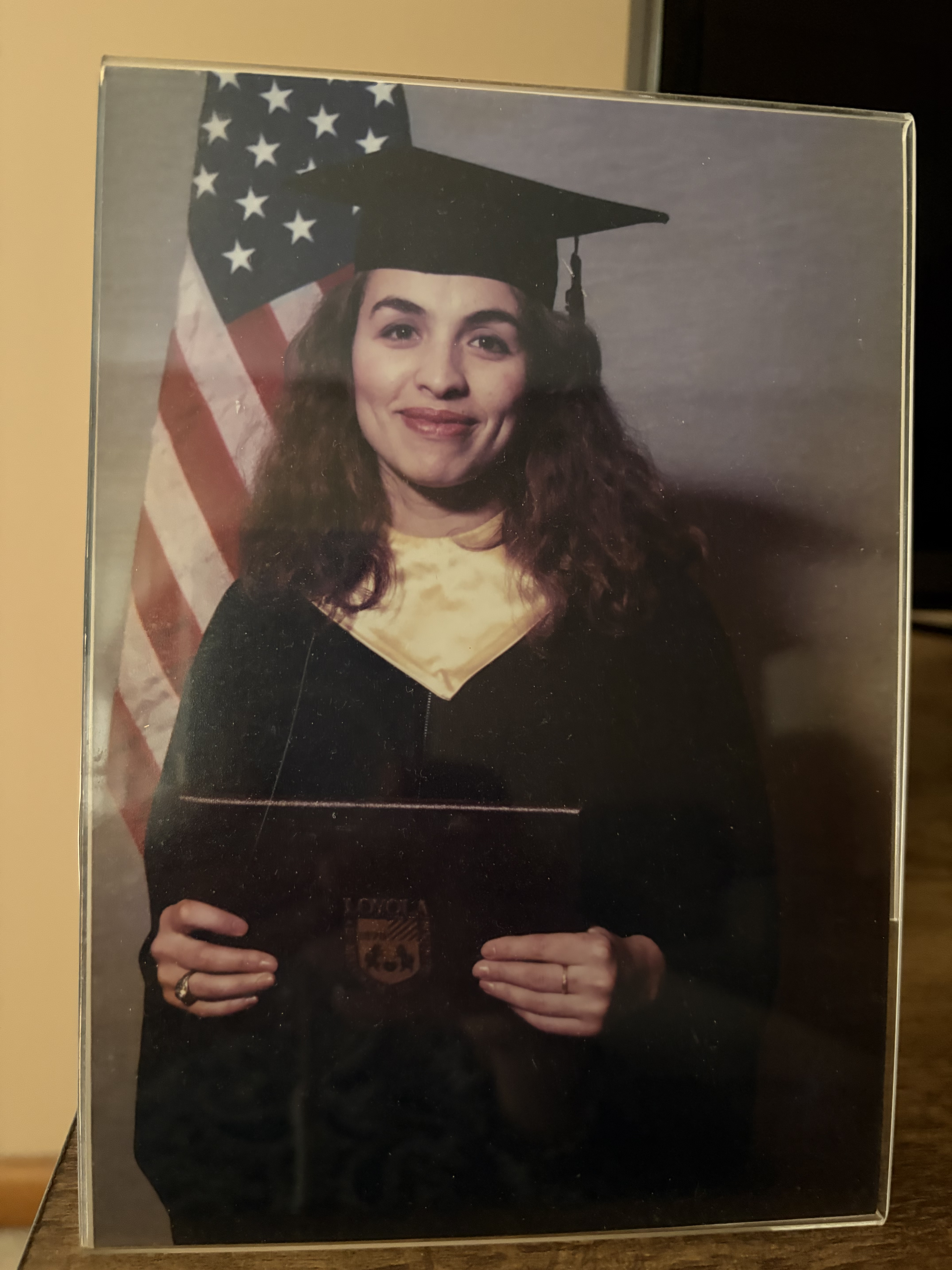 A young woman wearing graduation gear carrying a Loyola diploma